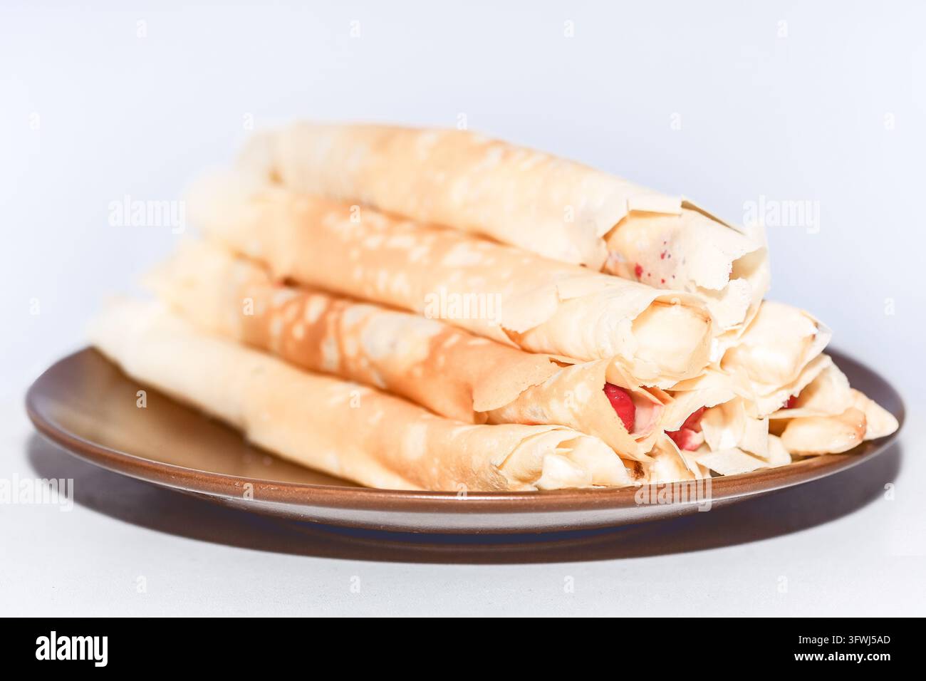 Pila di rotoli di sfoglia croccanti ripieni di pezzi di fragole fresche. Strati sottili e friabili sono arrotolati e disposti su un piatto di ceramica Foto Stock