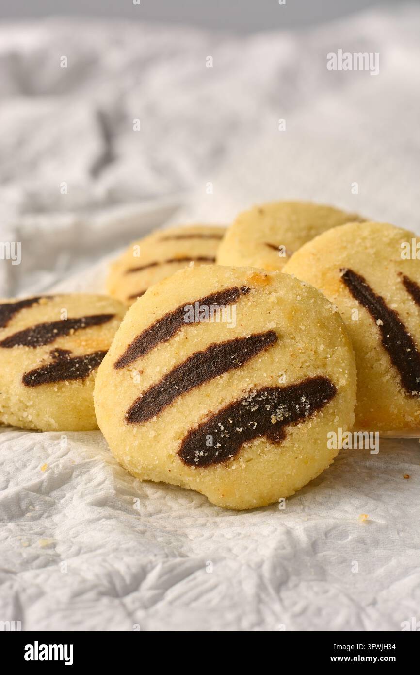 Biscotti rotondi con strisce di cioccolato e zucchero disposti su carta pergamena bianca spiegazzata. Biscotti sablati dolci con crosta di zucchero. Pasticceria fatta in casa. Foto Stock