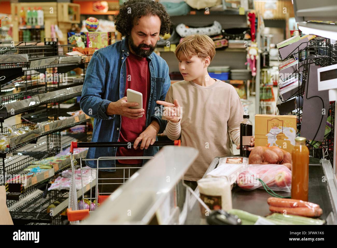 Padre di mezza età e ragazzo che controllano lo smartphone alla cassa del supermercato Foto Stock