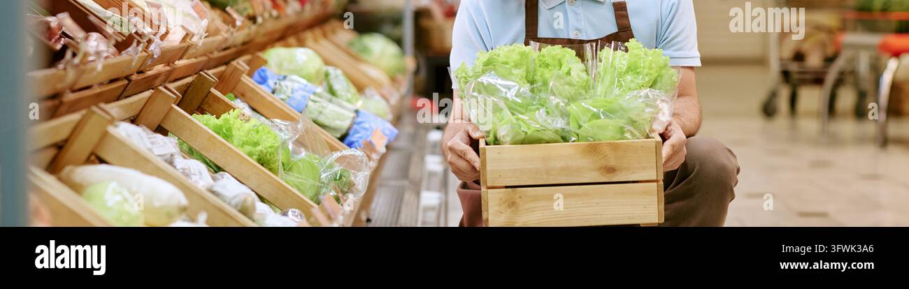 Intestazione di un dipendente del supermercato che tiene una cassa di legno con lattuga verde fresca Foto Stock