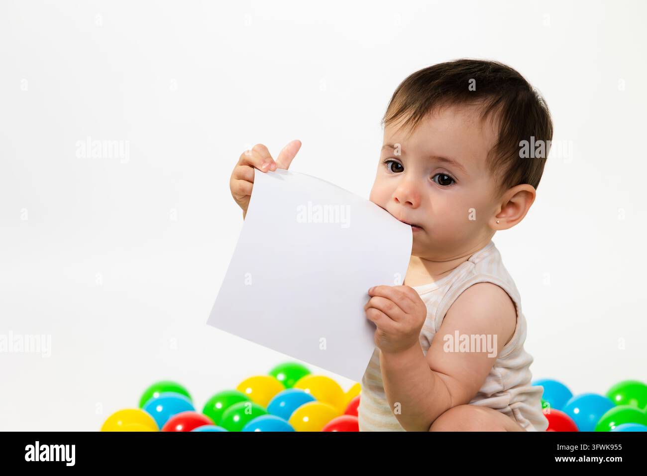 Bambino che mastica carta bianca con palline di plastica colorate Foto Stock