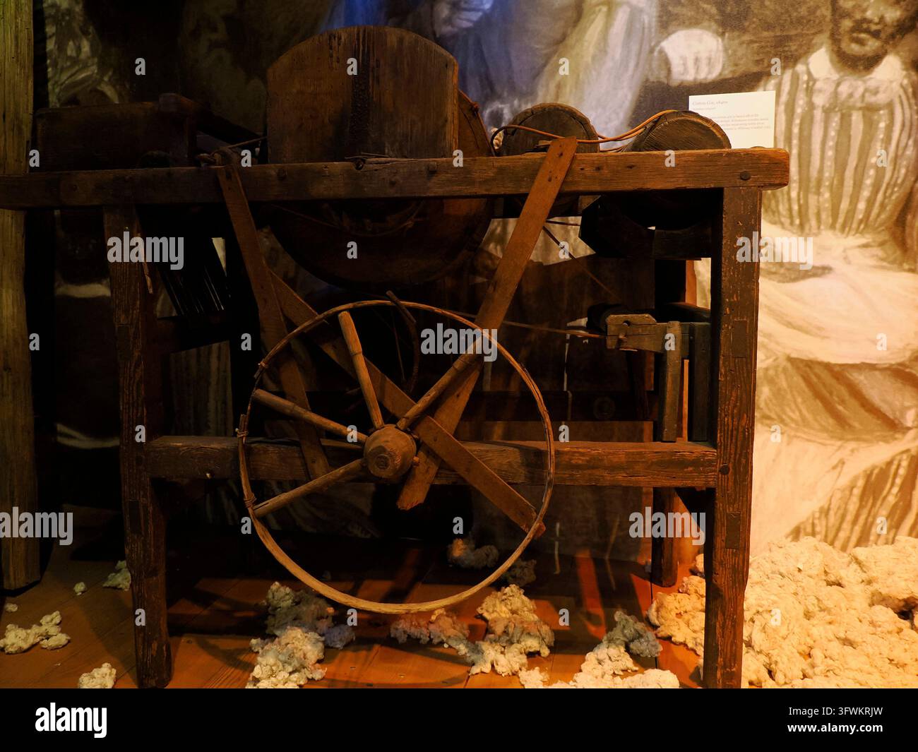 CINCINNATI, USA - 7 SETTEMBRE 2024: Macchina storica in legno per la sgranatura del cotone esposta in un museo della schiavitù, circondata da capsule di cotone grezzo con arte d'epoca Foto Stock