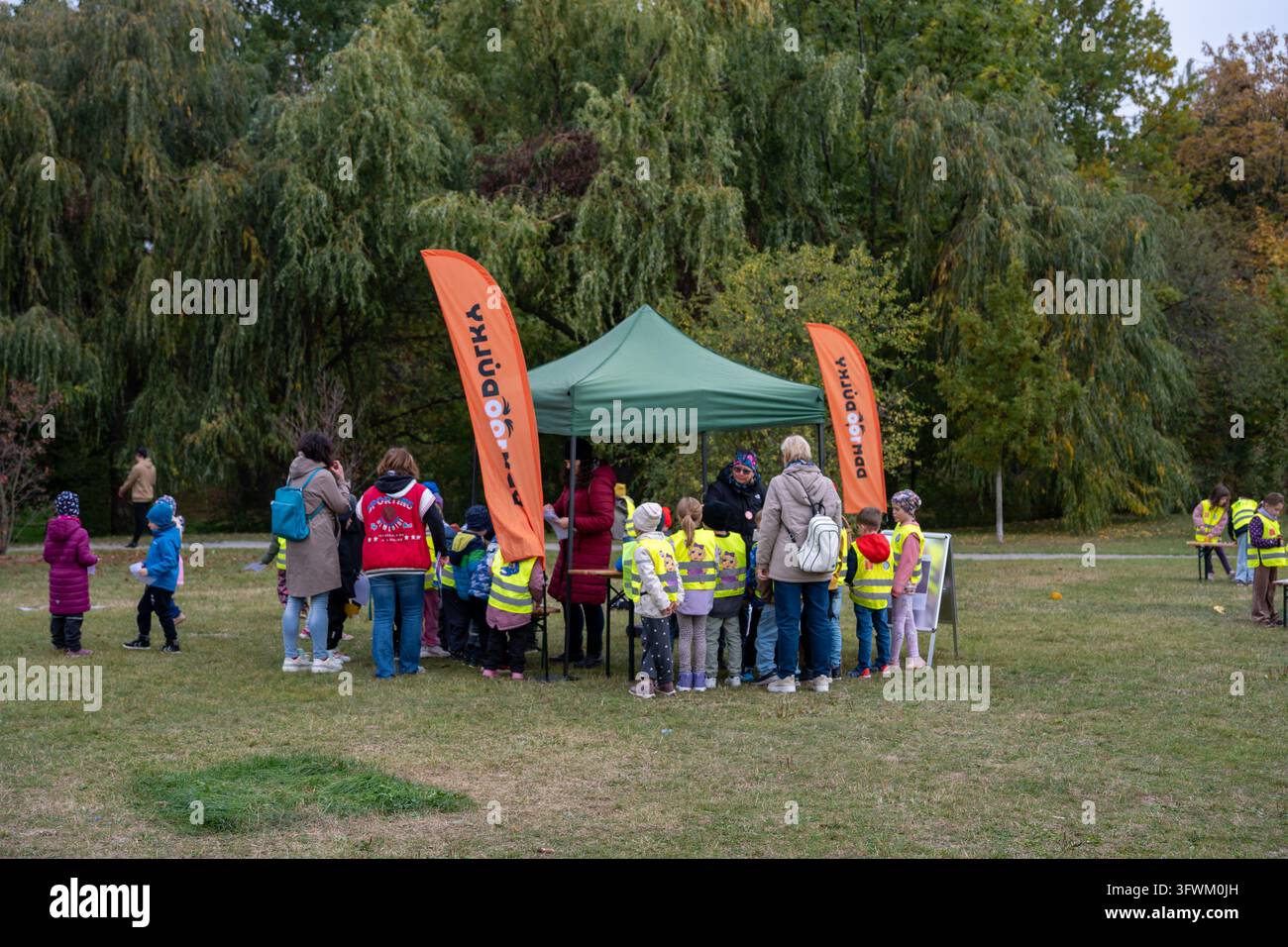 I bambini si radunano a uno stand di educazione naturale con bandiere promozionali arancioni durante l'evento Giornata dell'Albero a Praga 13. Foto Stock