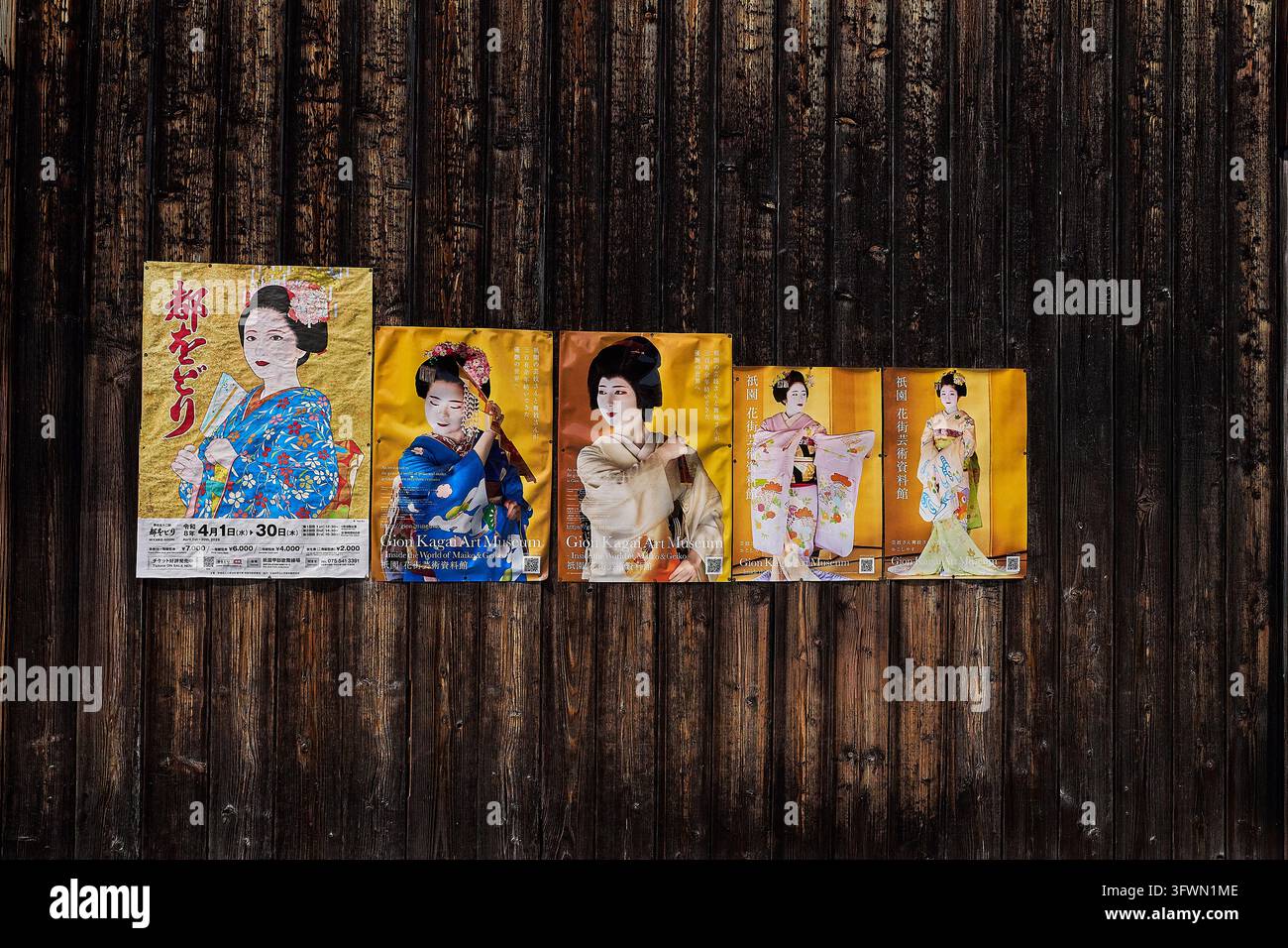 Poster colorati di geishe e maiko giapponesi in kimono tradizionale esposti su una parete di legno in Giappone, che promuovono la cultura giapponese. Foto Stock