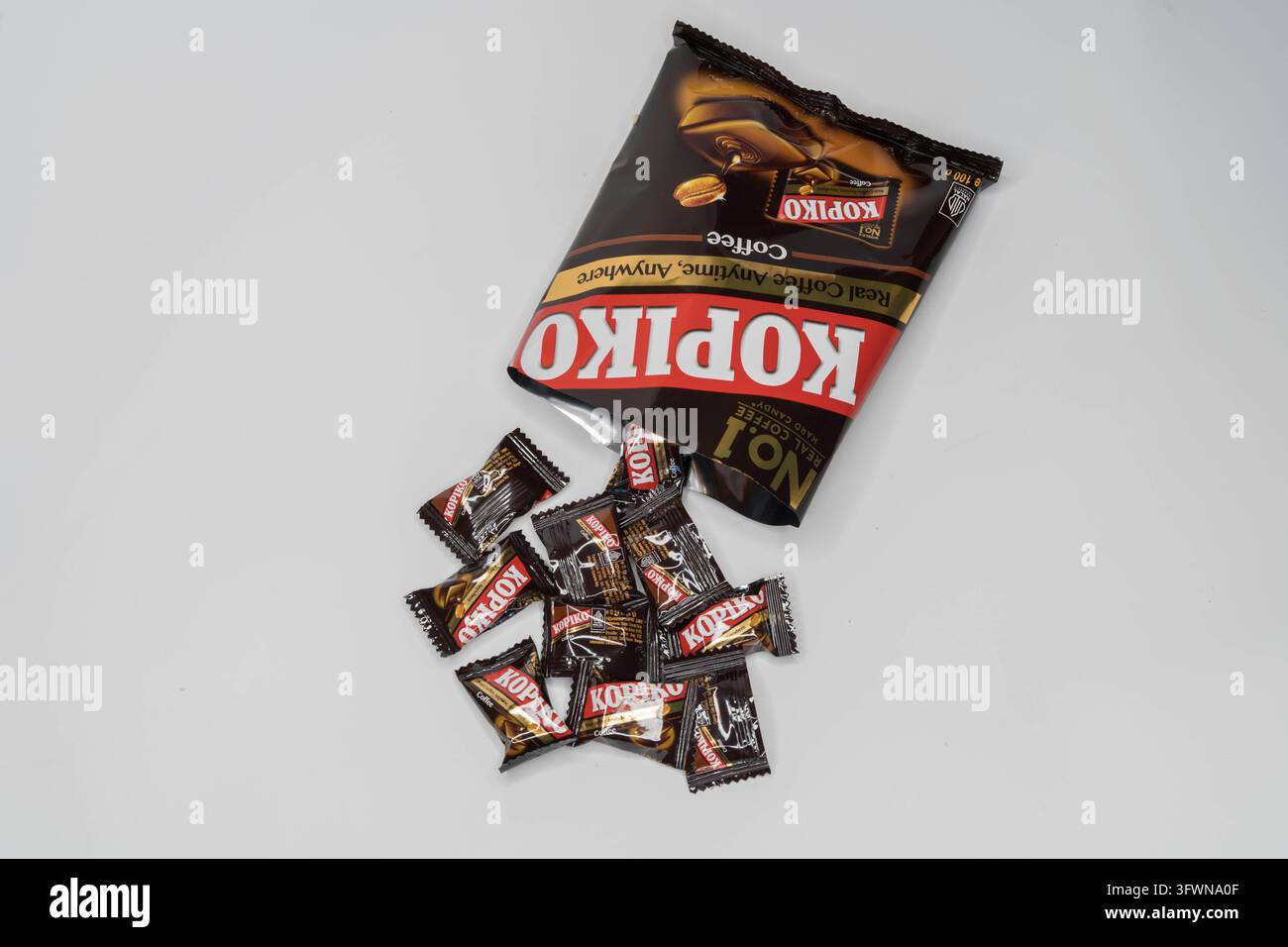 Caramelle al caffè Kopiko che fuoriescono da una busta aperta nera e marrone, con dolcetti confezionati singolarmente sparsi su uno sfondo bianco Foto Stock