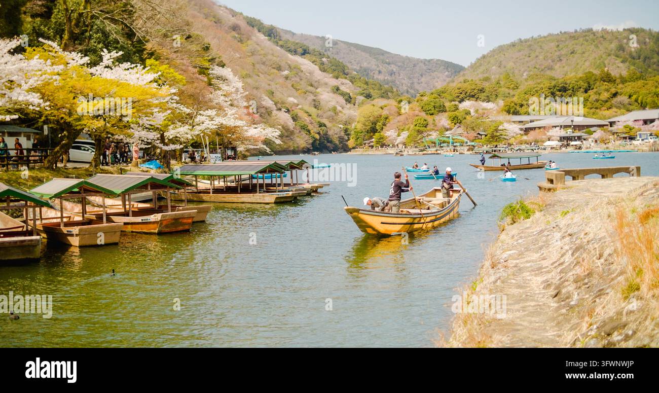 Kyoto, Prefettura di Kyoto, Giappone – 10 aprile 2025: Vista di Arashiyama con barche di legno tradizionali sul fiume Hozugawa, circondata da ciliegi in fiore Foto Stock