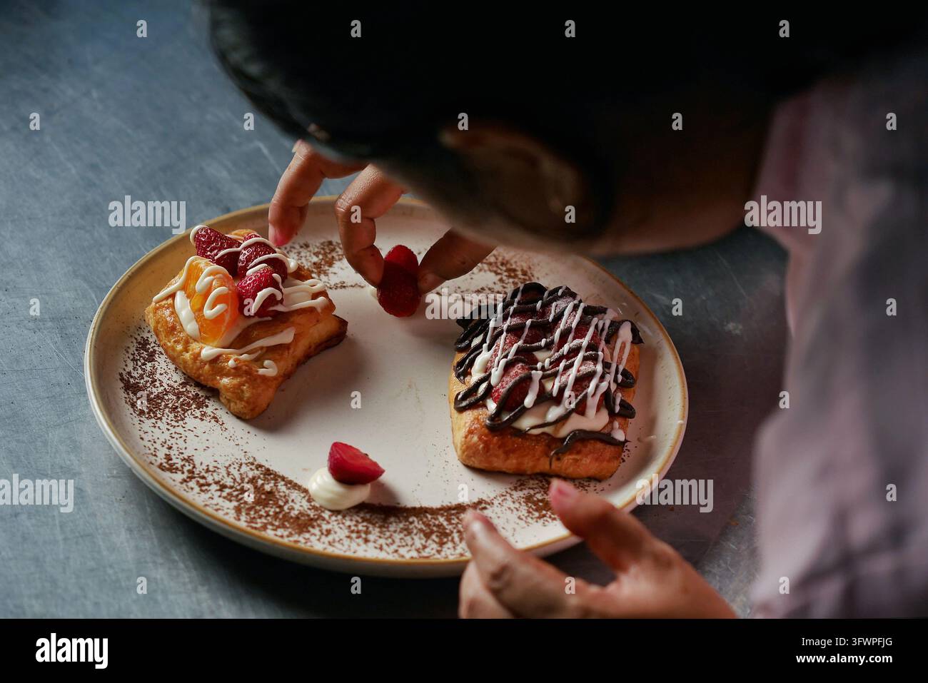 Stylista alimentare, disponi un piatto di dessert a forma di toast con guarnizione di fragole fresche, salsa al cioccolato e panna su un piatto bianco. Foto Stock