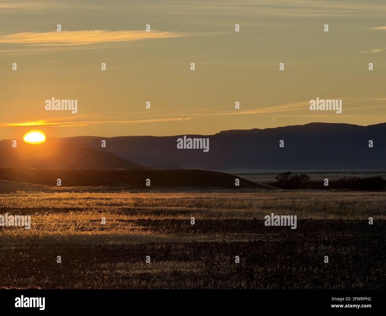 Il sole arancione tramonta dietro creste montuose stratificate oltre una pianura desertica aperta vicino a Sossusvlei, Namibia. - Immagine stock catturata con smartphone