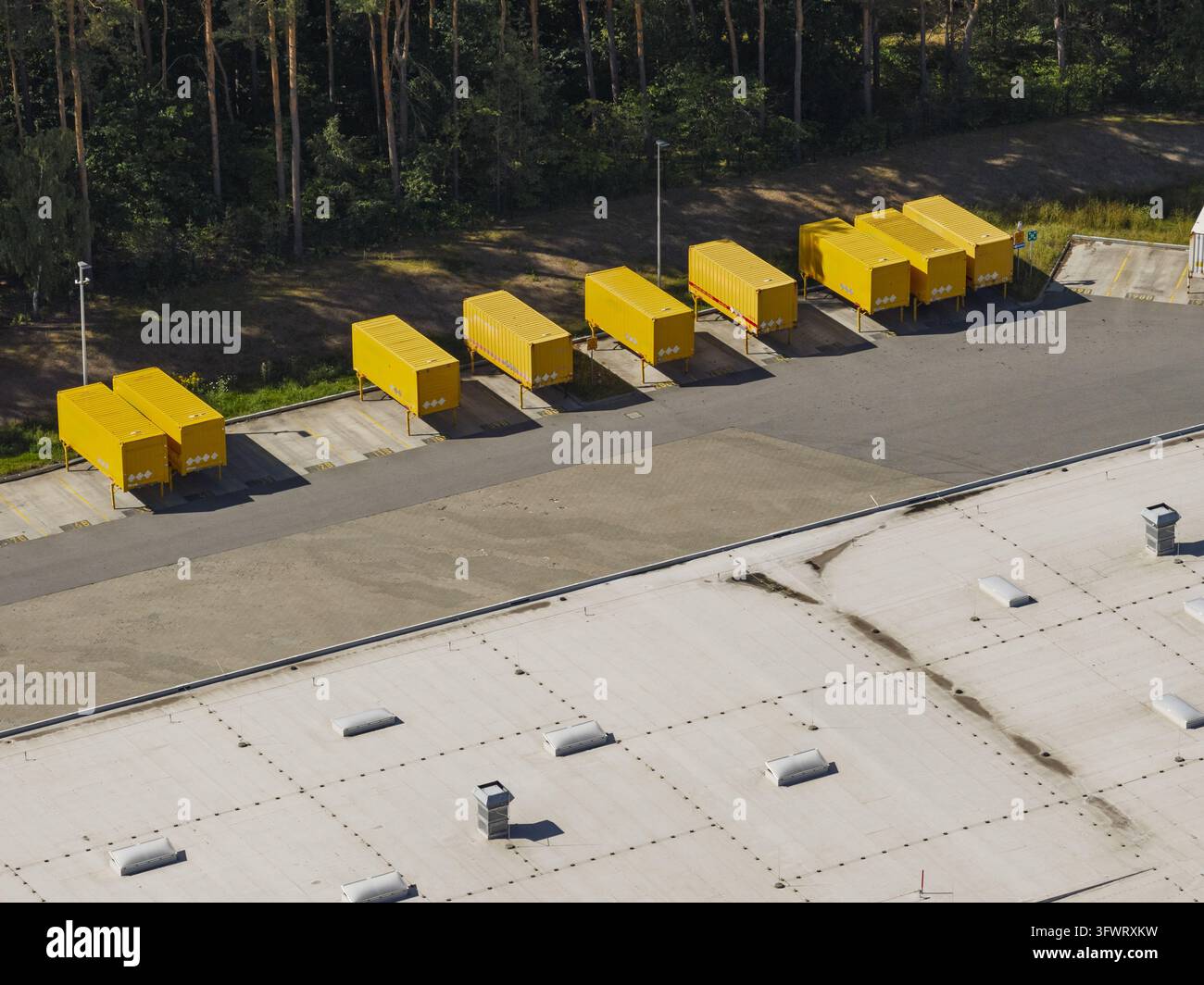 Vista aerea di container di spedizione gialli parcheggiati in fila in una struttura logistica accanto a un grande edificio industriale con tetto piatto a Neustrelitz Foto Stock