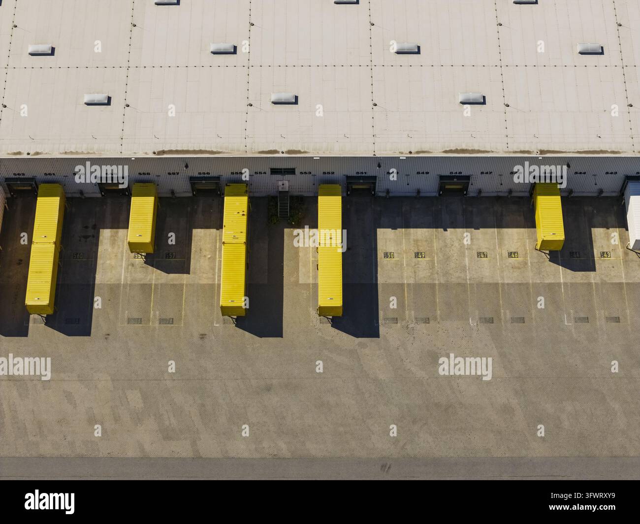 Vista aerea di un molo di carico di un magazzino con rimorchi gialli parcheggiati alle banchine, cortile in cemento e tetto di un edificio industriale, Neustrelitz, Meclemburgo-Pomerania Anteriore Foto Stock