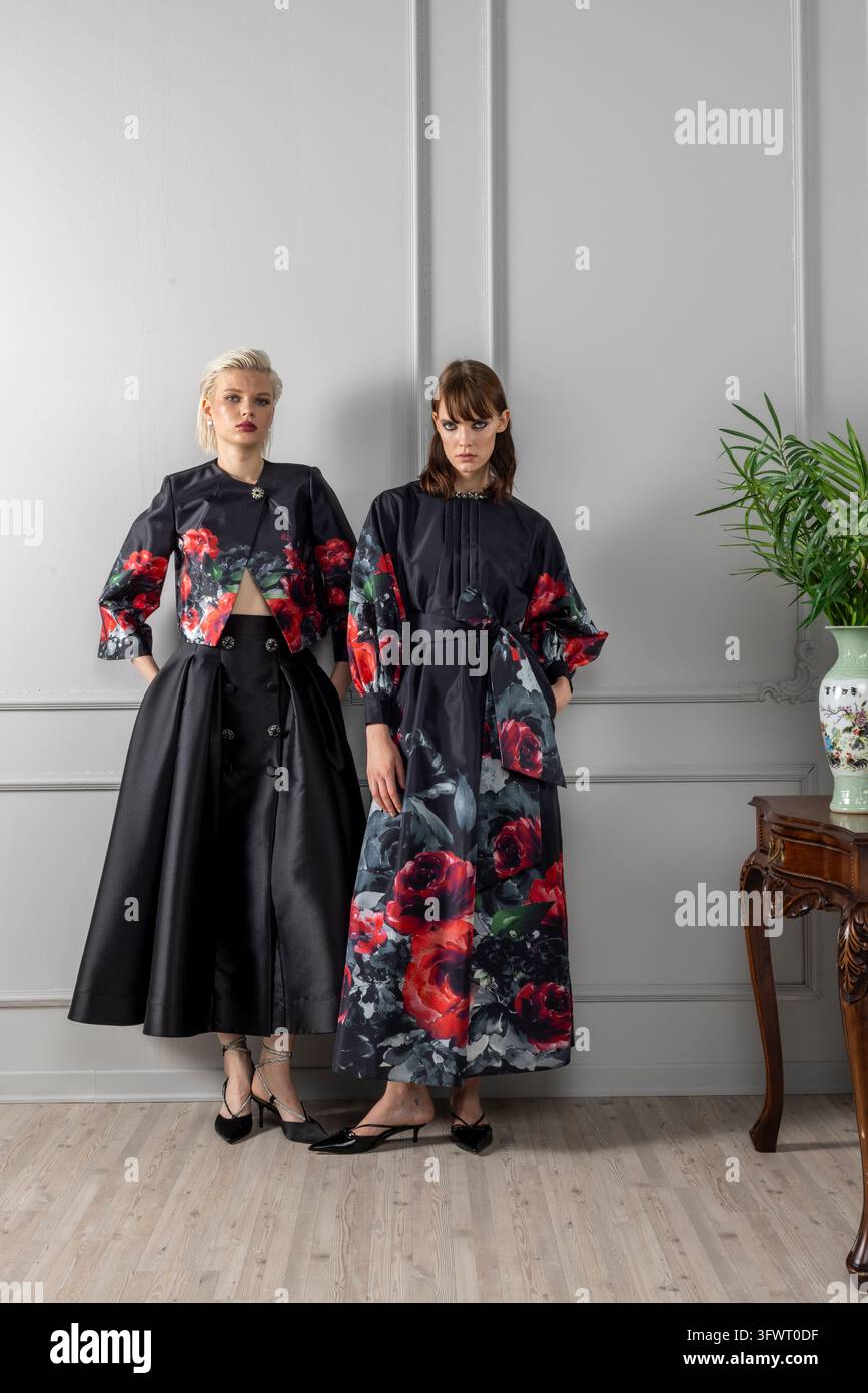 Scatto verticale di due modelli con stampe di rose nere coordinate, una giacca floreale corta con gonna interamente abbottonata e un lungo vestito floreale con cintura. Foto Stock
