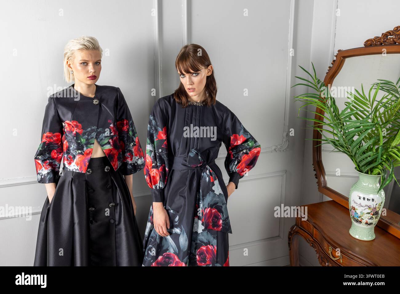 Scatto orizzontale dalla vita verso l'alto di due modelli, uno con una giacca nera corta con rose rosse e gonna ampia, l'altro con un vestito a stampa rosa con corpetto a pinces. Foto Stock