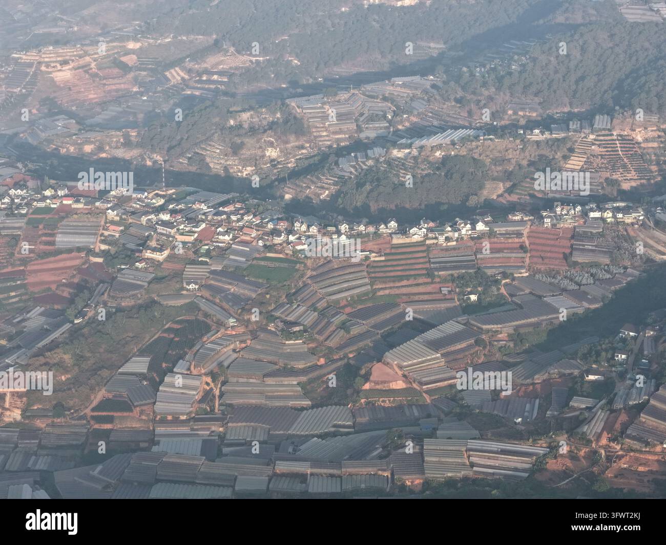 Vista aerea di serre a terrazzo e campi agricoli incastonati tra le colline ondulate e il paesaggio urbano di Da Lat, Lam Dong, Vietnam. Foto Stock
