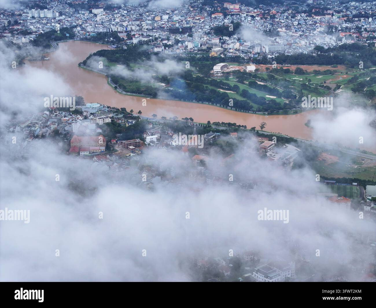 Vista aerea del lago Xuan Huong circondato da colline ondulate, nuvole dense e il paesaggio urbano di Da Lat, Lam Dong, Vietnam. Foto Stock