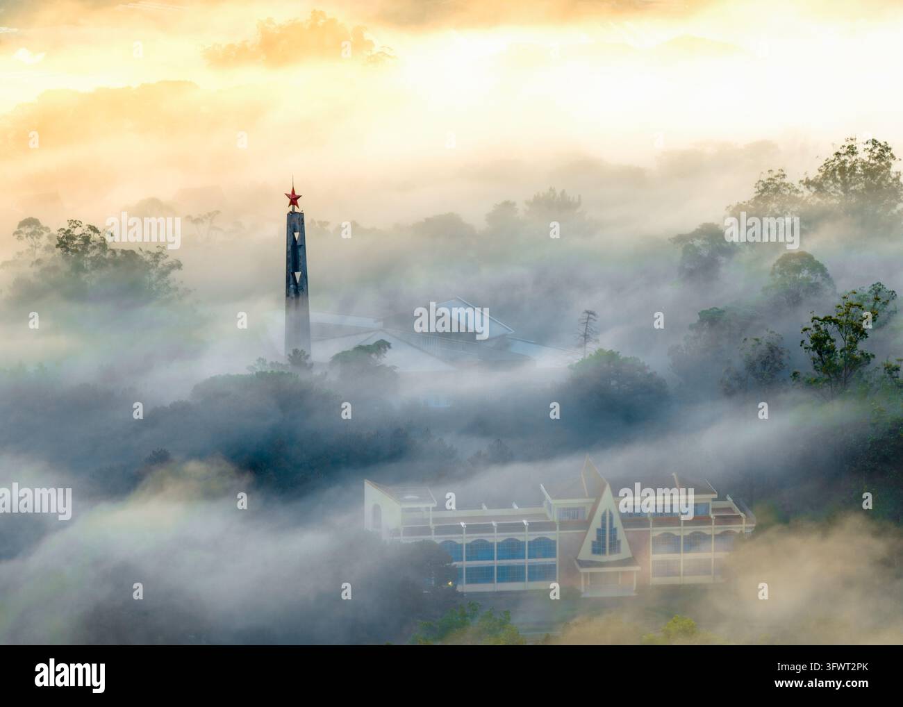 Vista aerea della torre iconica del Collegio Pedagogico di Da Lat che emerge dalla fitta nebbia mattutina sulla foresta circostante a Da Lat, Lam Dong, Vietnam Foto Stock