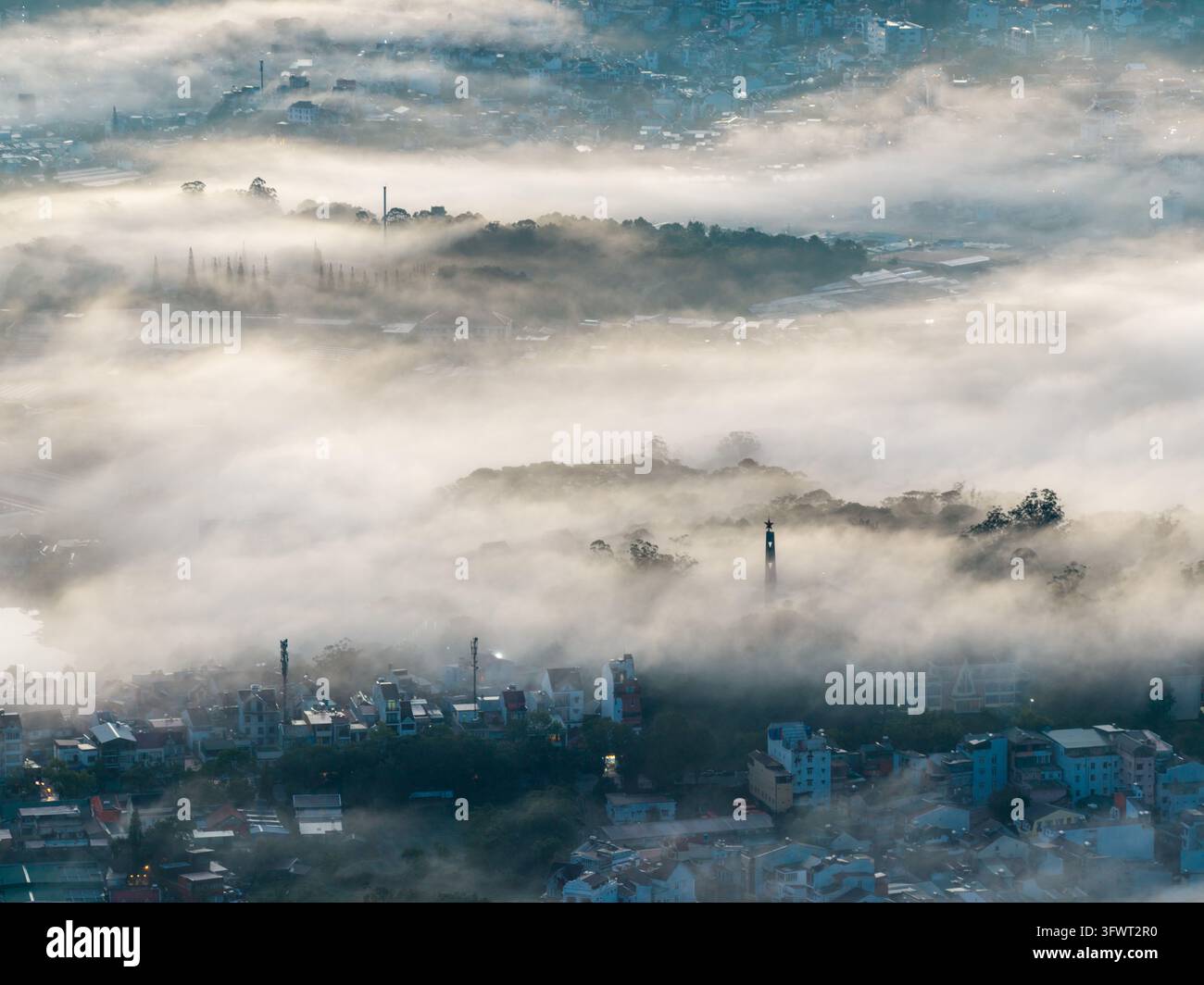 Vista aerea della città di Da Lat parzialmente oscurata da una fitta nebbia mattutina con tetti e alberi lussureggianti visibili nella luce del primo mattino a Da Lat, Lam Dong, Vietnam Foto Stock
