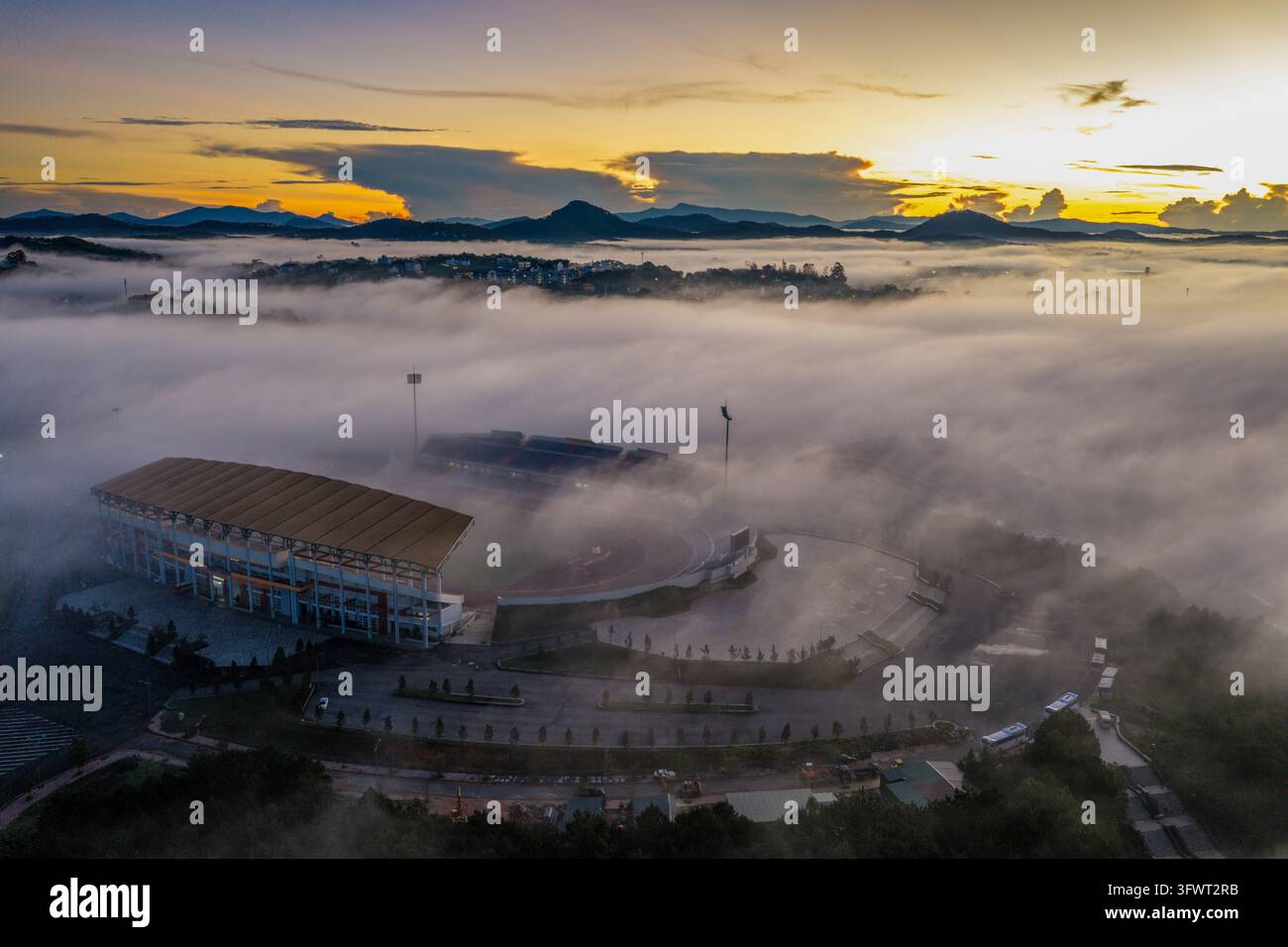 Vista aerea dello stadio di Da Lat circondato da una fitta nebbia mattutina con montagne sullo sfondo all'alba a Da Lat, Lam Dong, Vietnam. Foto Stock