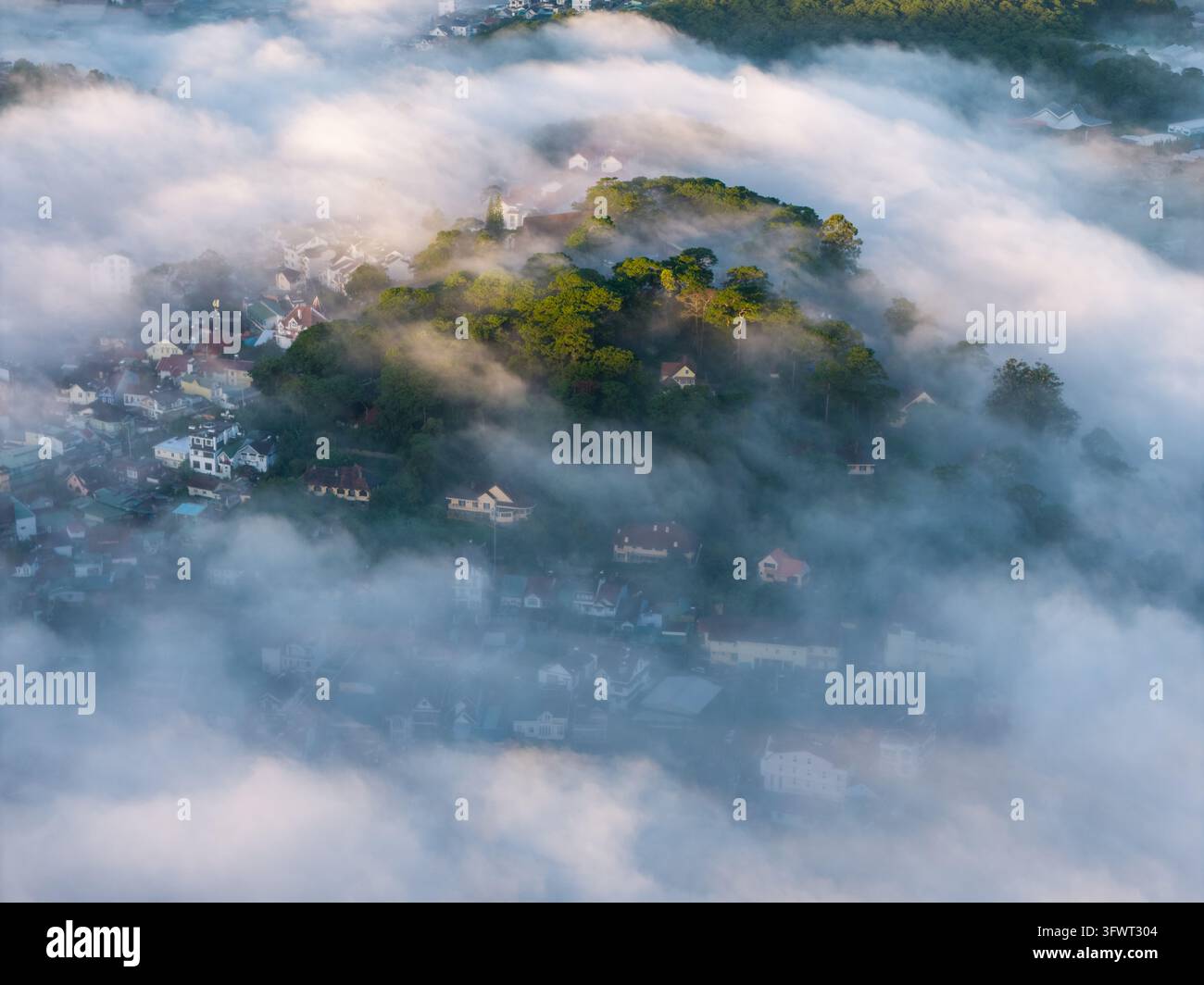 Vista aerea della città di Da Lat che emerge da una fitta nebbia mattutina con colline ricoperte di pini, tetti colorati e case incastonate nella valle a Da Foto Stock