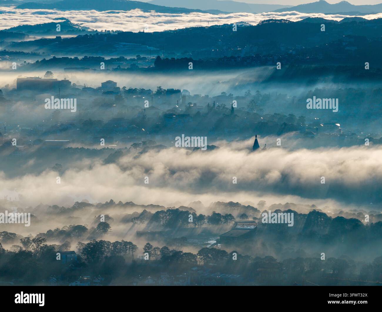Vista aerea di un paesaggio nebbioso con una fitta nebbia che copre la città, i pini e i tetti all'alba a Da Lat, Lam Dong, Vietnam Foto Stock