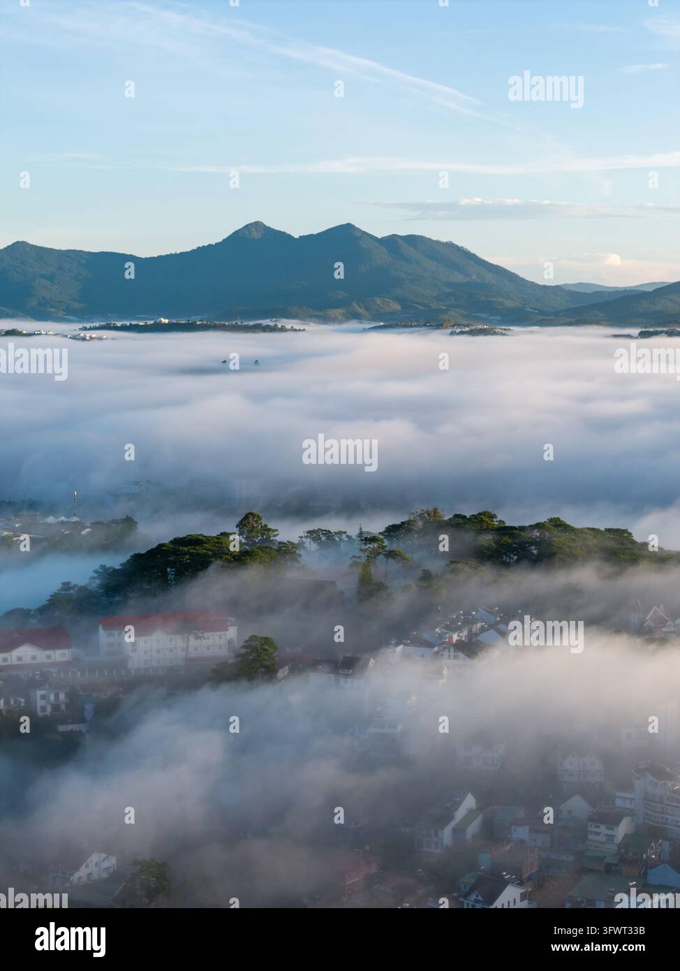 Vista aerea della città di Da Lat avvolta da una fitta nebbia mattutina con montagne sullo sfondo e tetti che affiorano attraverso la nebbia a Da Lat, Lam Dong, Vietnam Foto Stock