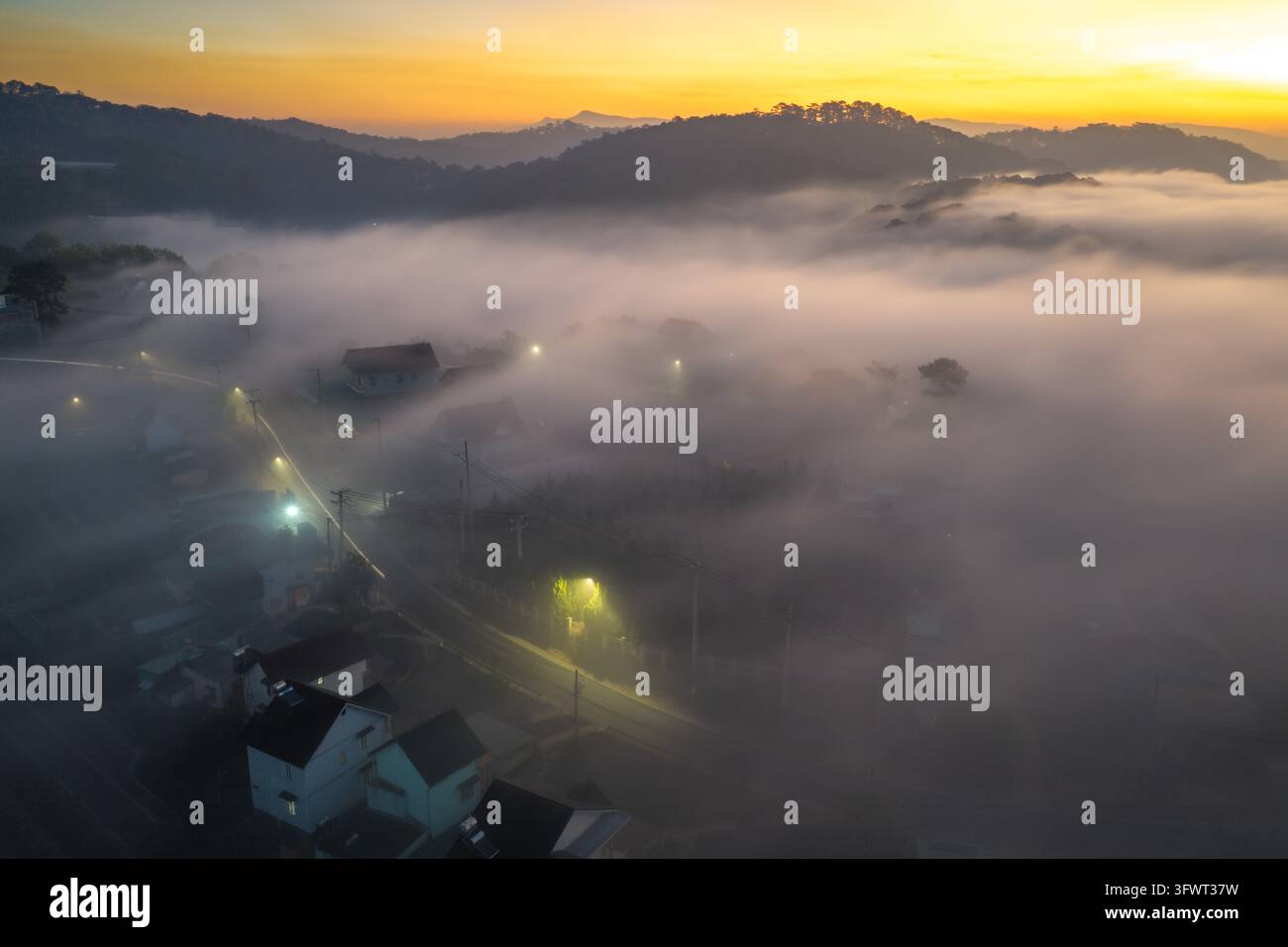 Vista aerea della città all'alba con nebbia fitta, lampioni illuminati e case incastonate nelle colline di Da Lat, Lam Dong, Vietnam. Foto Stock