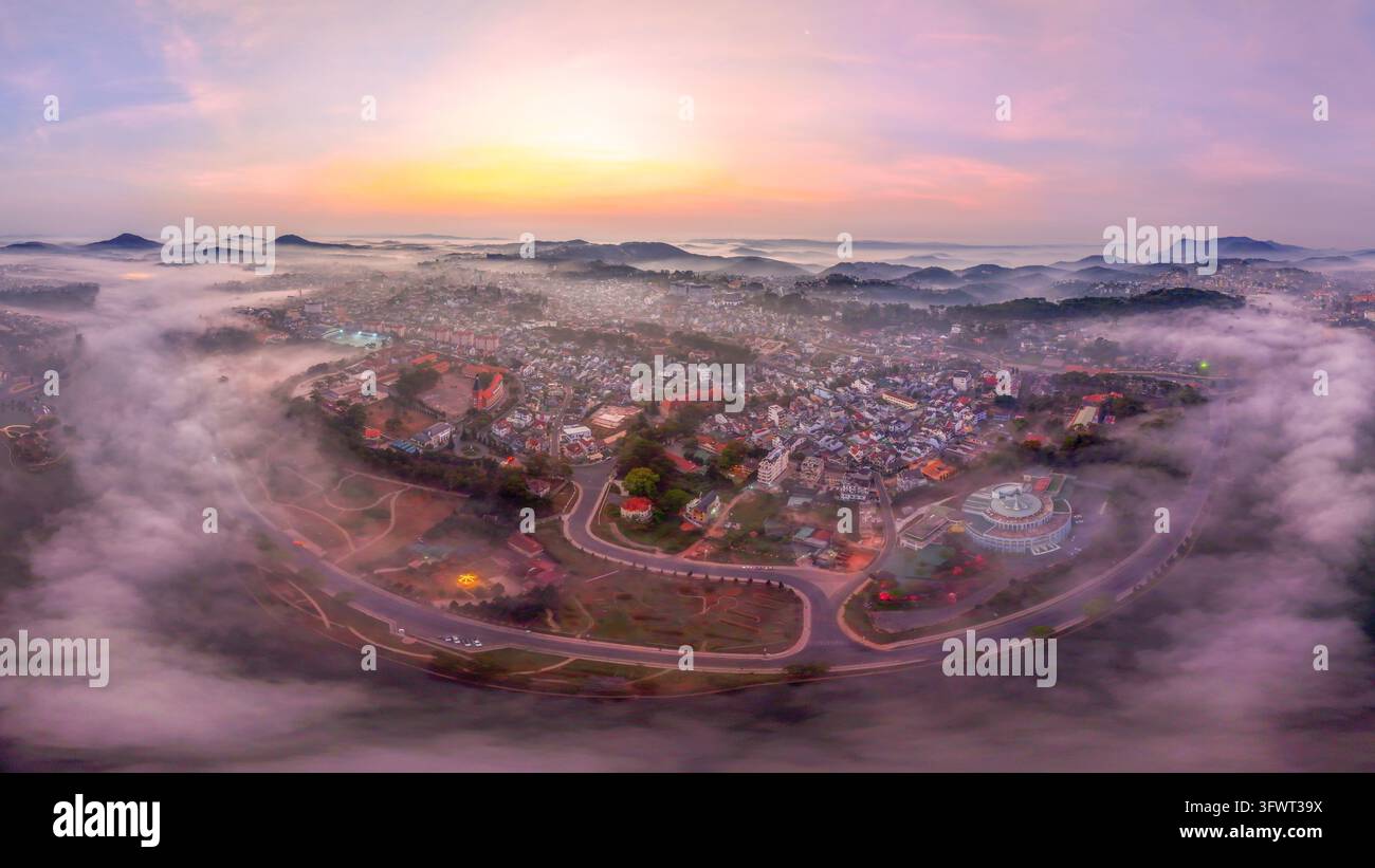 Vista aerea del lago Xuan Huong circondato dal paesaggio urbano brumoso di Da Lat all'alba con dolci colline e luce mattutina soffusa a Da Lat, Lam D Foto Stock