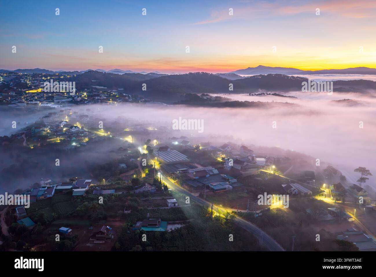 Vista aerea della città di Da Lat all'alba con una fitta nebbia che copre la valle, lampioni luminosi e colline ondulate sullo sfondo, Da Lat, Lam Dong Foto Stock