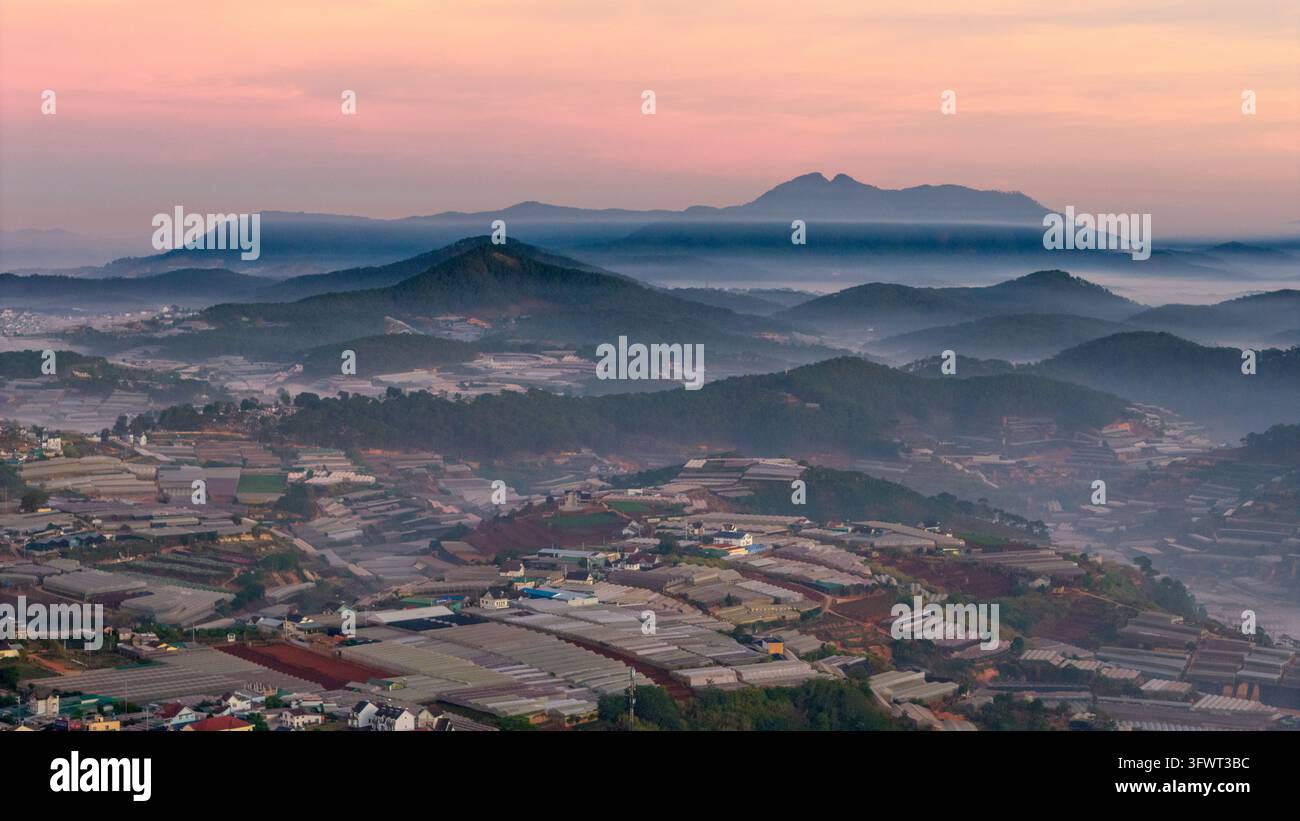 Vista aerea di serre che coprono le colline ondulate di Da Lat all'alba con montagne nebbiose sullo sfondo, Da Lat, Lam Dong, Vietnam. Foto Stock