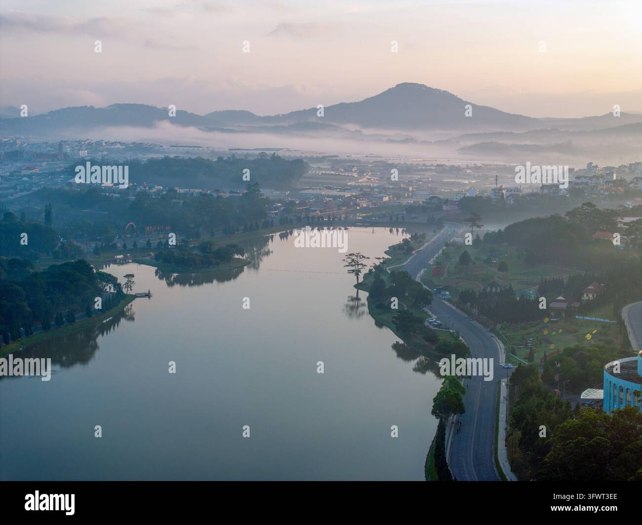 Vista aerea del lago Xuan Huong circondato da una vegetazione lussureggiante e montagne nebbiose al mattino presto a Da Lat, Lam Dong, Vietnam. Foto Stock