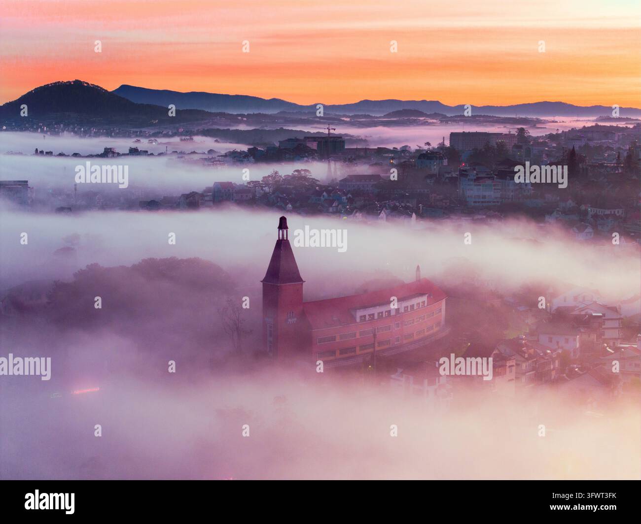 Veduta aerea del Collegio Pedagogico di Da Lat che si erge sopra uno spesso strato di nebbia mattutina con montagne in lontananza all'alba a Da Lat, Lam Do Foto Stock