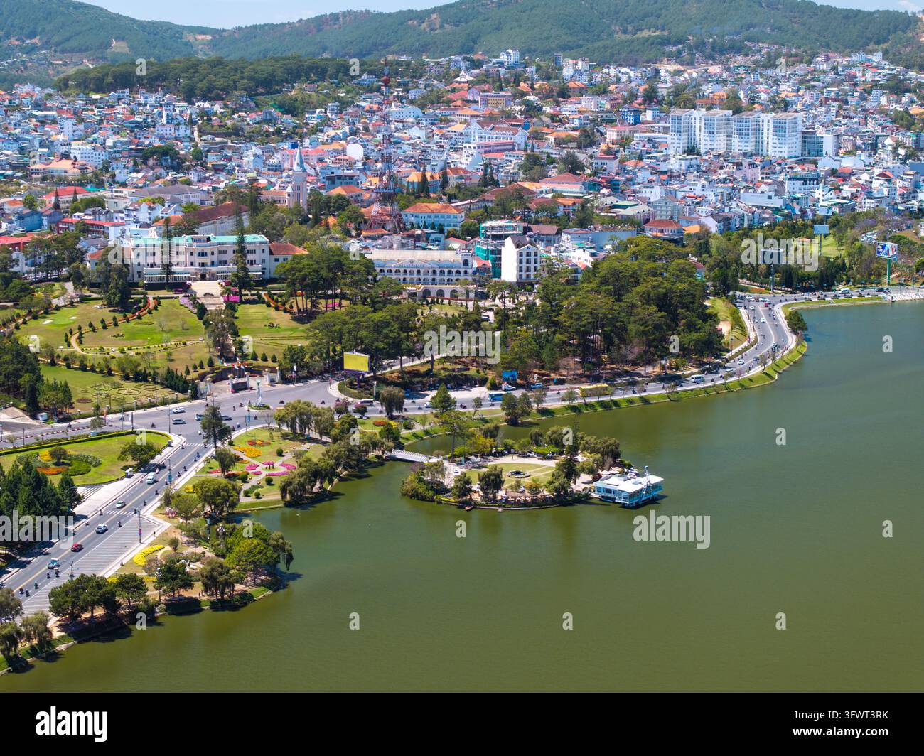Vista aerea del lago Xuan Huong circondato da una vegetazione lussureggiante, strade tortuose e il paesaggio urbano collinare di Da Lat, Lam Dong, Vietnam. Foto Stock