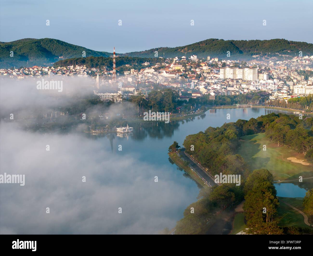 Vista aerea del lago Xuan Huong circondato dalla nebbia mattutina, dalle foreste di pini e dalla città collinare di Da Lat nel Lam Dong, Vietnam. Foto Stock