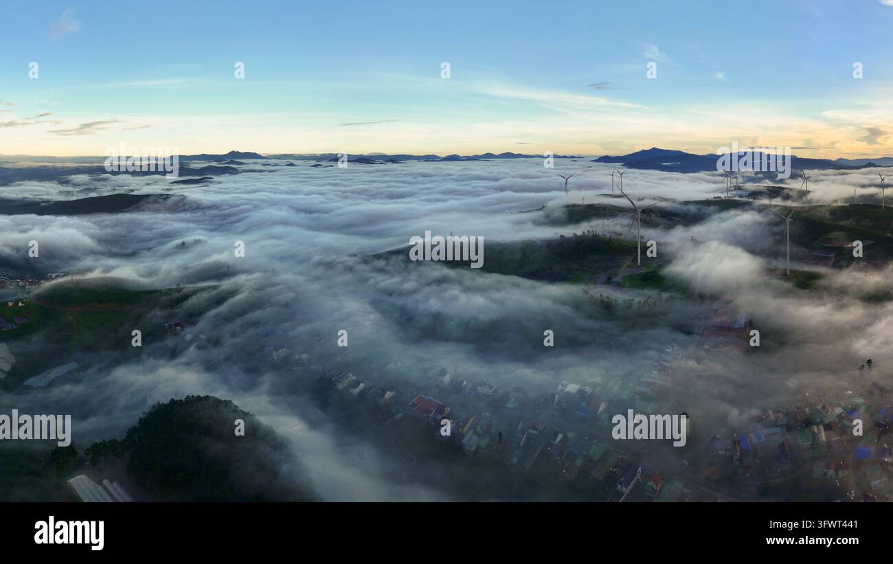 Vista aerea di turbine eoliche che si ergono sopra uno spesso strato di nebbia mattutina che copre la valle e le case a Da Lat, Lam Dong, Vietnam. Foto Stock