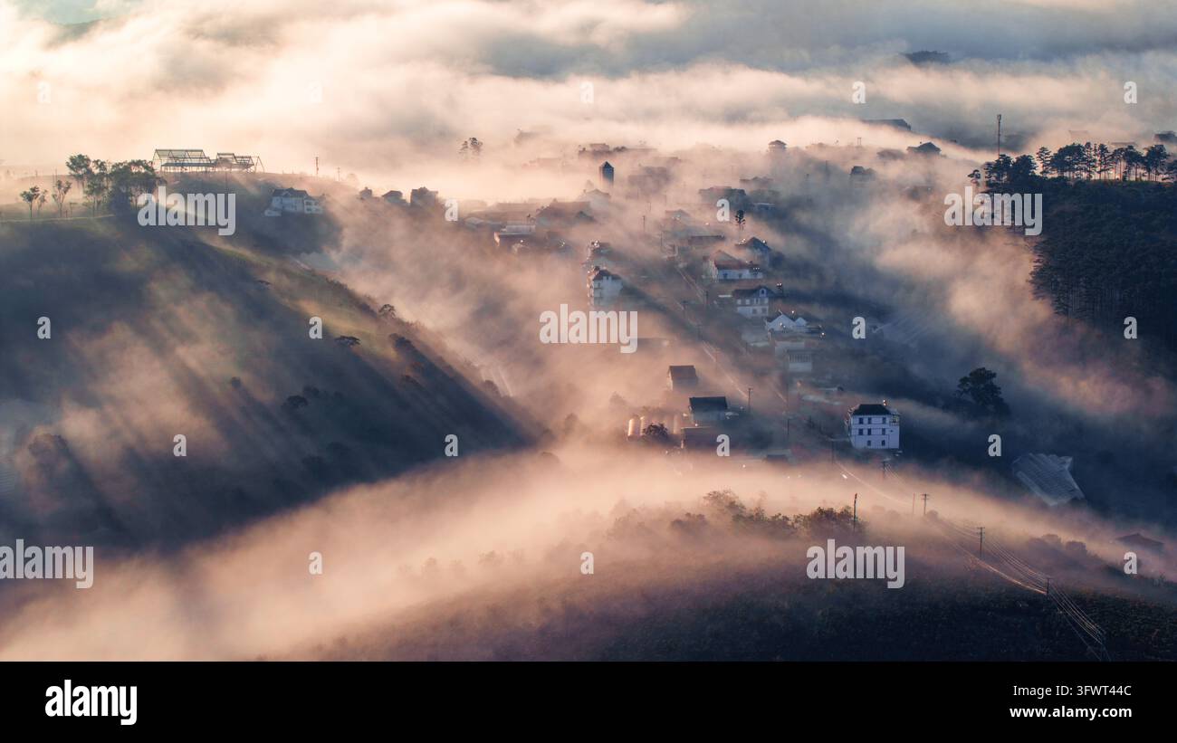 Vista aerea del paesaggio nebbioso di Da Lat con case incastonate tra colline ondulate e pini durante l'ora dorata a Da Lat, Lam Dong, Vietnam. Foto Stock