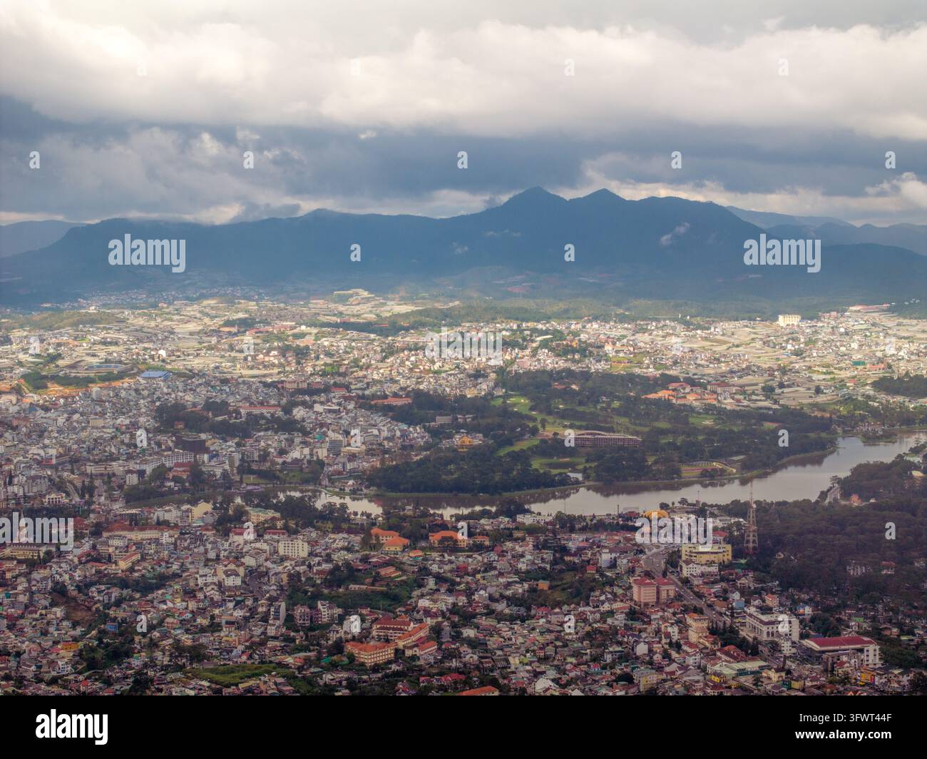 Vista aerea della città di Da Lat con il lago Xuan Huong, tetti urbani fitti e montagne circostanti sotto un cielo nuvoloso a Da Lat, Lam Dong, Vietnam Foto Stock