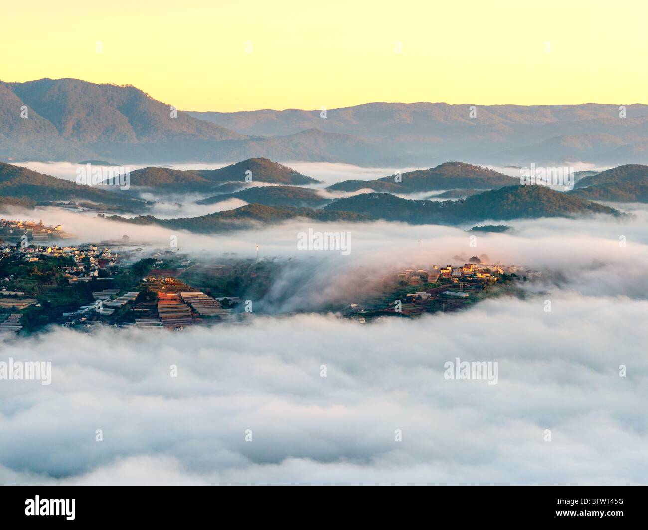 Vista aerea della valle nebbiosa con serre e montagne ondulate all'alba a Da Lat, Lam Dong, Vietnam. Foto Stock