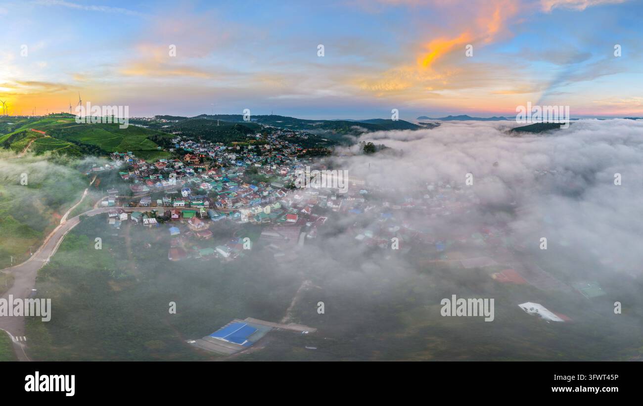 Vista aerea della città di Da Lat incastonata tra colline ondulate e fitta nebbia durante un vivido tramonto con tetti colorati e strade tortuose, Da Lat, Lam Don Foto Stock