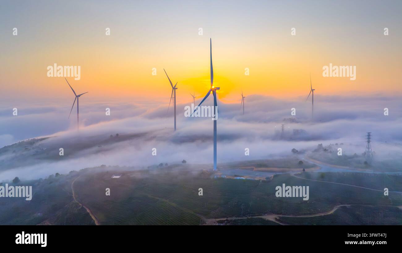 Veduta aerea di turbine eoliche che si ergono sopra un mare di nuvole all'alba, con luce dorata che illumina il paesaggio a Da Lat, Lam Dong, Vietnam. Foto Stock