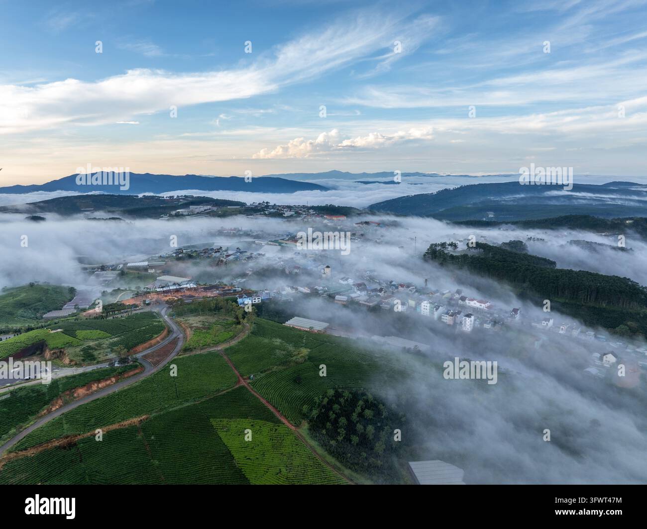 Vista aerea della città di Da Lat annidata tra colline ondulate e lussureggianti piantagioni di tè, parzialmente oscurata da una spessa coltre di nebbia mattutina, Da Lat Foto Stock