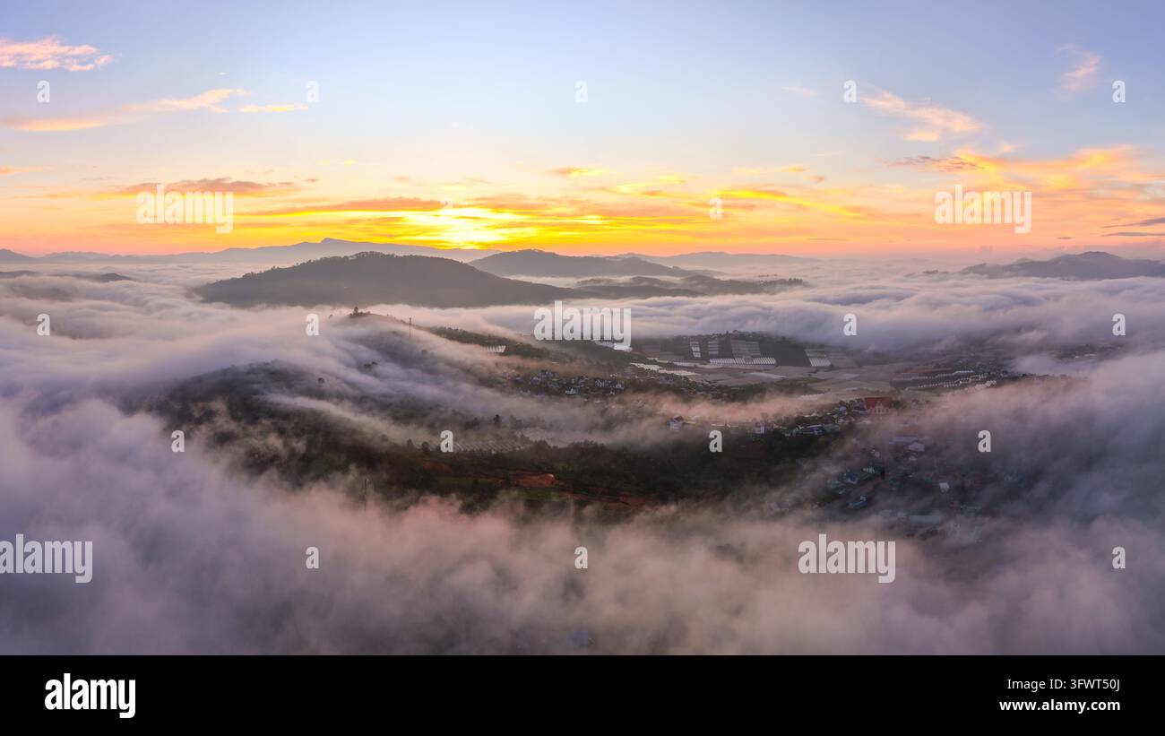 Vista aerea del paesaggio nebbioso di Da Lat all'alba, con dolci colline che emergono da una spessa coltre di nuvole sotto un cielo dorato a Da Lat, Lam Đồng Foto Stock