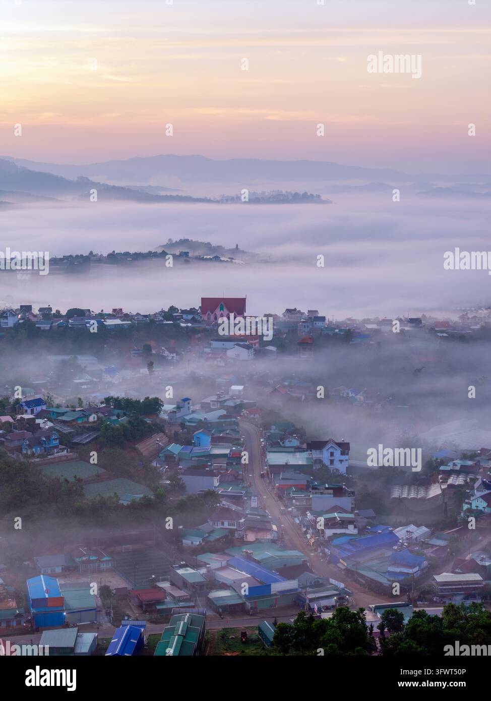 Veduta aerea della città di Da Lat incastonata nelle colline brumose delle Terre Alte Centrali con tetti colorati e una chiesa prominente che emerge dal Foto Stock