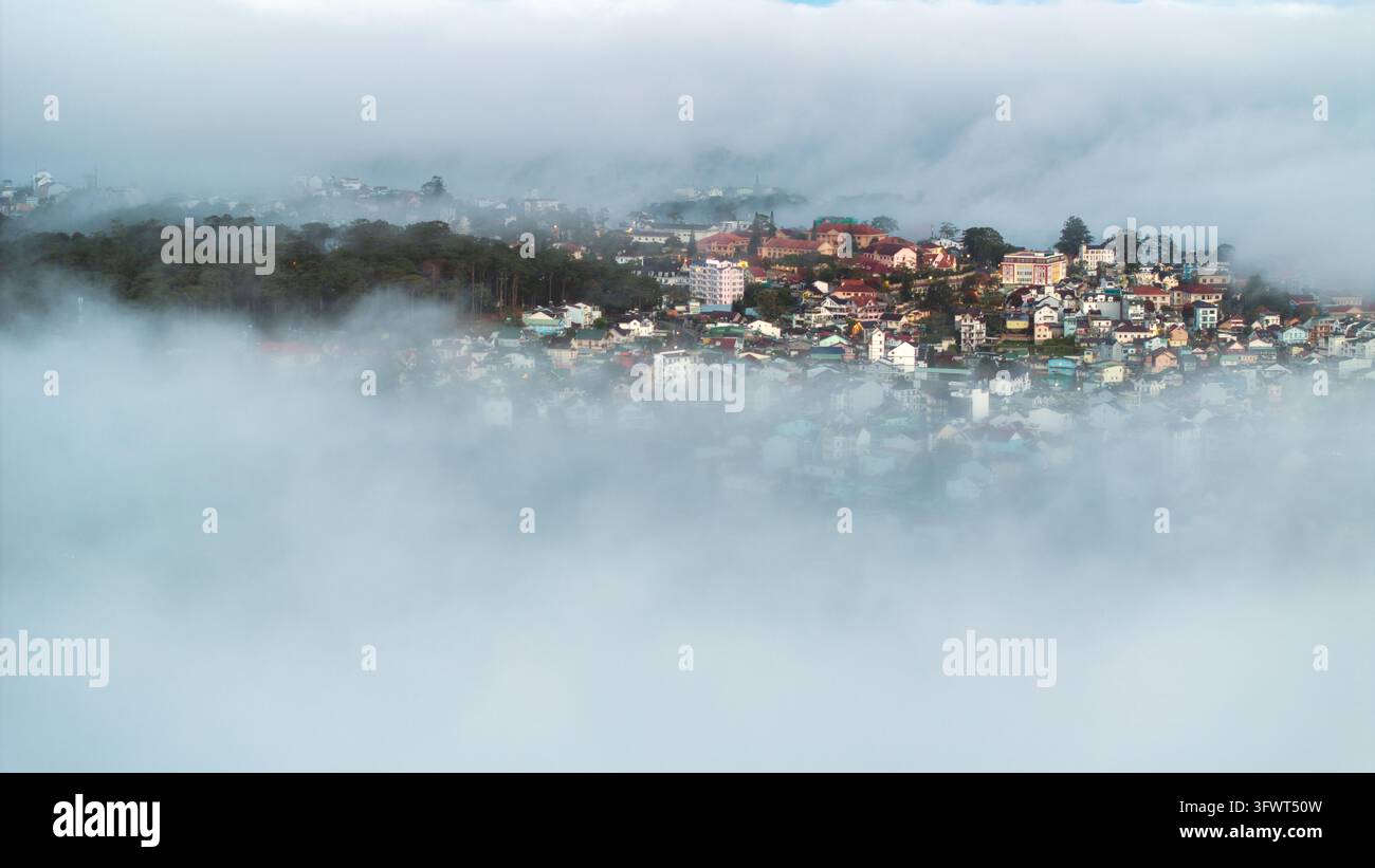 Vista aerea di case colorate e foreste di pini parzialmente oscurate da una fitta nebbia mattutina a Da Lat, Lam Dong, Vietnam. Foto Stock