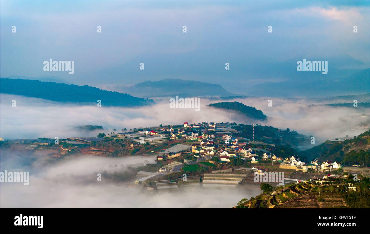 Vista aerea della città di Da Lat annidata tra le montagne e coperta dalla nebbia mattutina, con numerose serre e edifici residenziali a Da Foto Stock