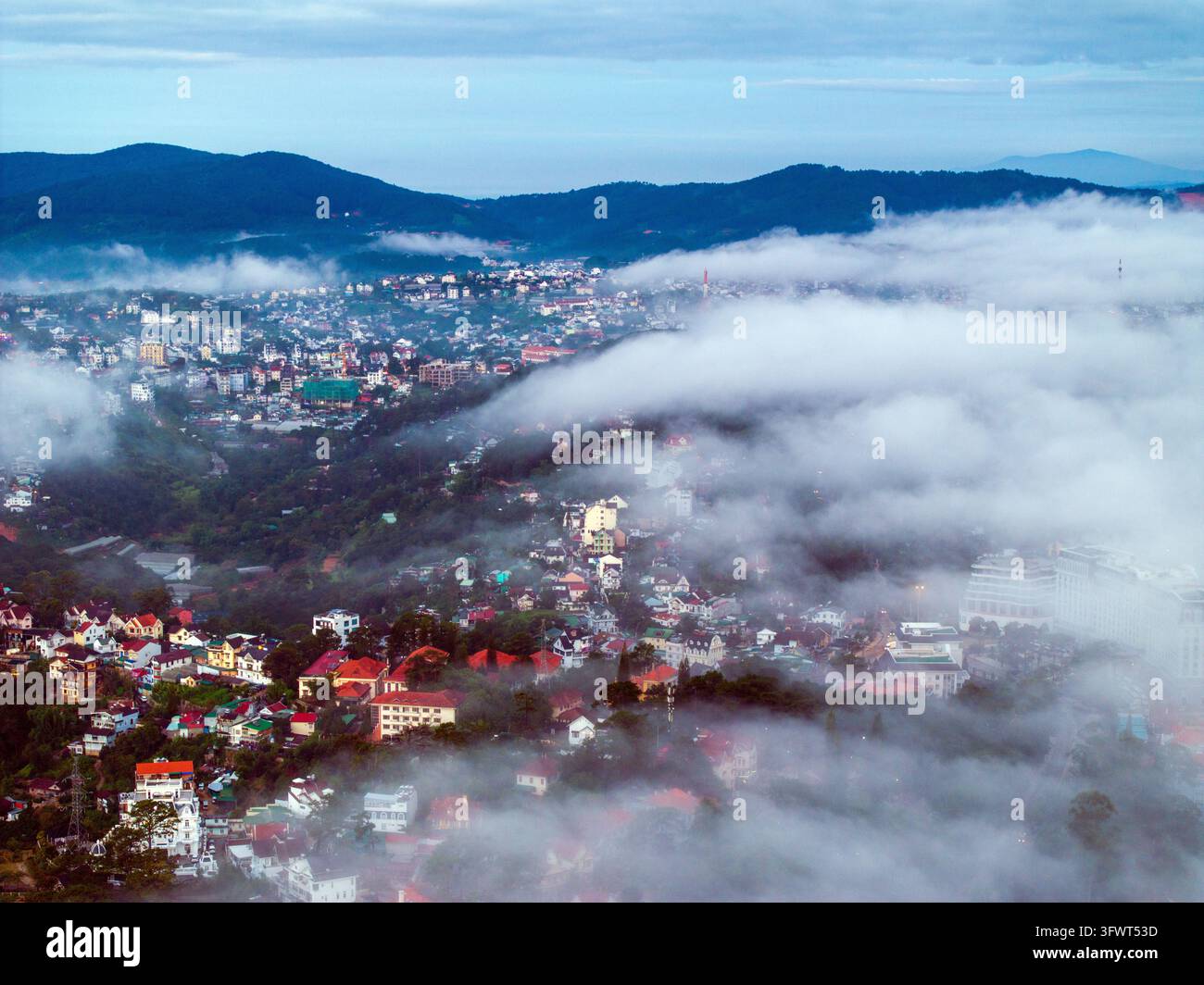 Vista aerea della città di Da Lat incastonata tra le montagne con tetti colorati che emergono attraverso una fitta nebbia mattutina e colline ondulate a Da Lat, Lam Đăng Foto Stock