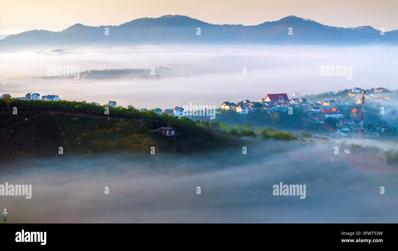 Vista aerea del paesaggio nebbioso con case incastonate tra colline sotto una luce mattutina soffusa a Da Lat, Lam Dong, Vietnam. Foto Stock