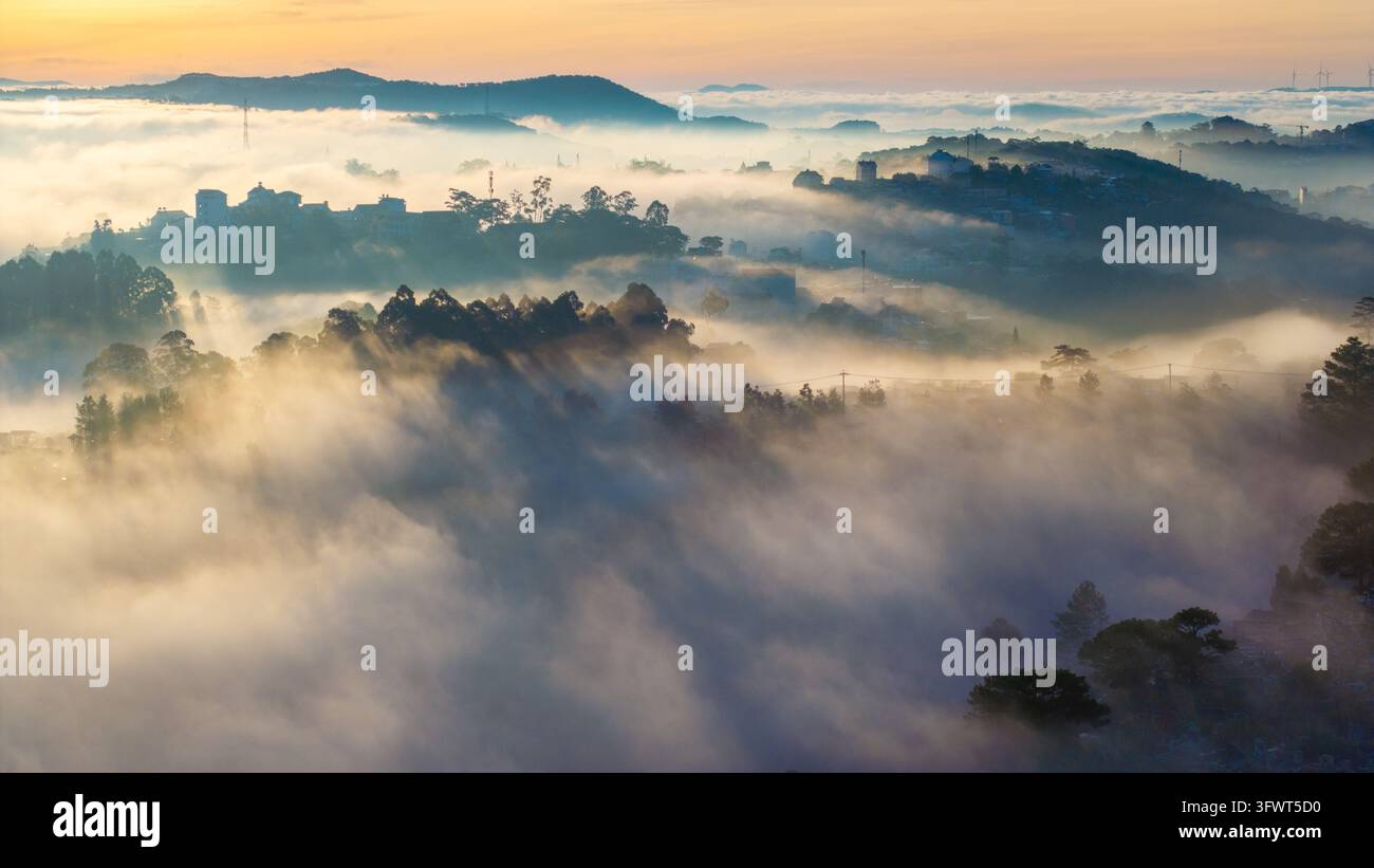 Vista aerea del paesaggio nebbioso di Da Lat all'alba con una fitta nebbia che copre le colline, i pini e gli edifici lontani a Da Lat, Lam Dong, Vietnam Foto Stock
