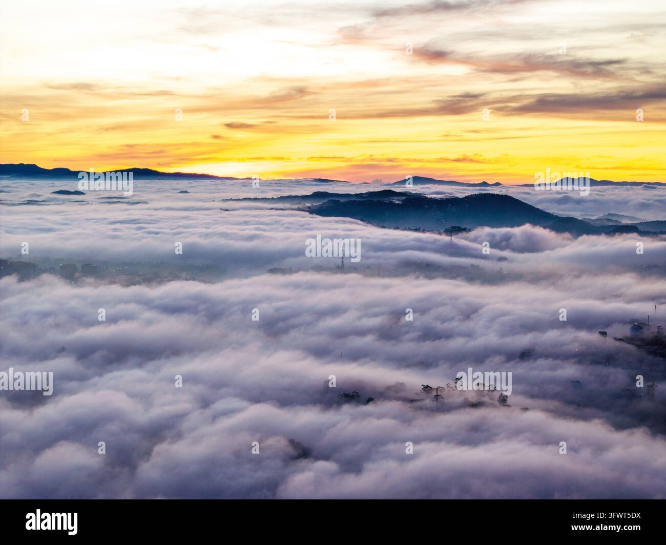 Vista aerea di un mare di nuvole che copre il paesaggio montano all'alba, con le cime degli alberi e le colline lontane che emergono dalla nebbia, Da Lat, Lam Dong Foto Stock