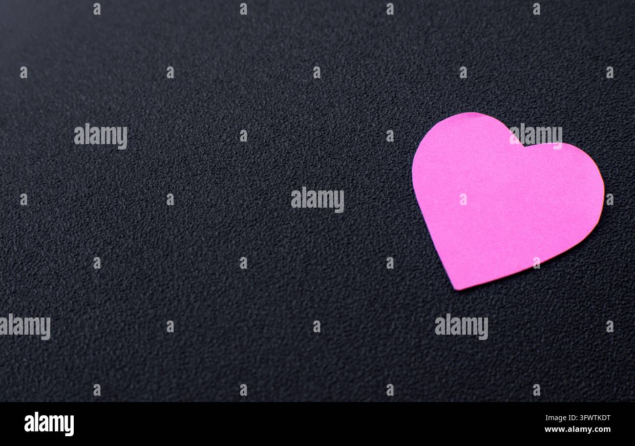 Cuore di carta rosa su uno sfondo nero scuro minimale, che crea un'immagine concettuale semplice per l'amore, il romanticismo, l'affetto e i temi emotivi. Foto Stock