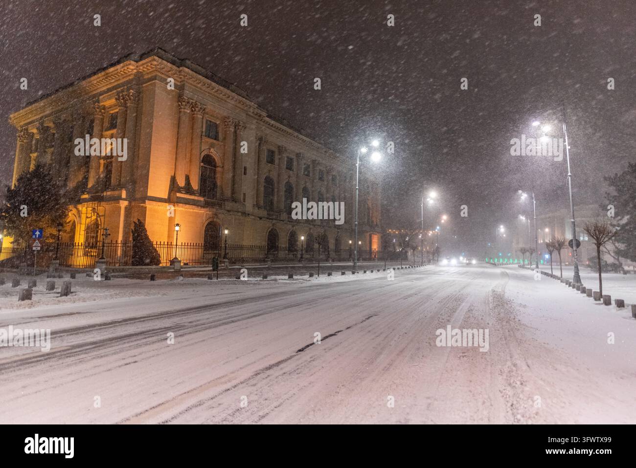 Vista del Museo Nazionale d'Arte della Romania illuminato di notte durante una forte nevicata, con strade coperte di neve e lampioni a Bucarest, B Foto Stock