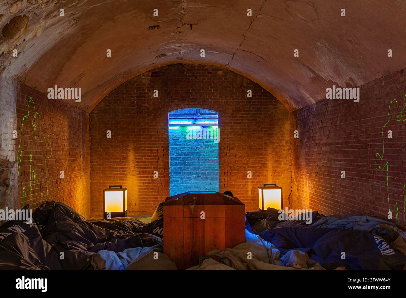Vista dell'interno di una casamatta storica in mattoni al Fort Pampus con una struttura in legno, pouf, lanterne e proiezioni di luce al neon a Goois Foto Stock